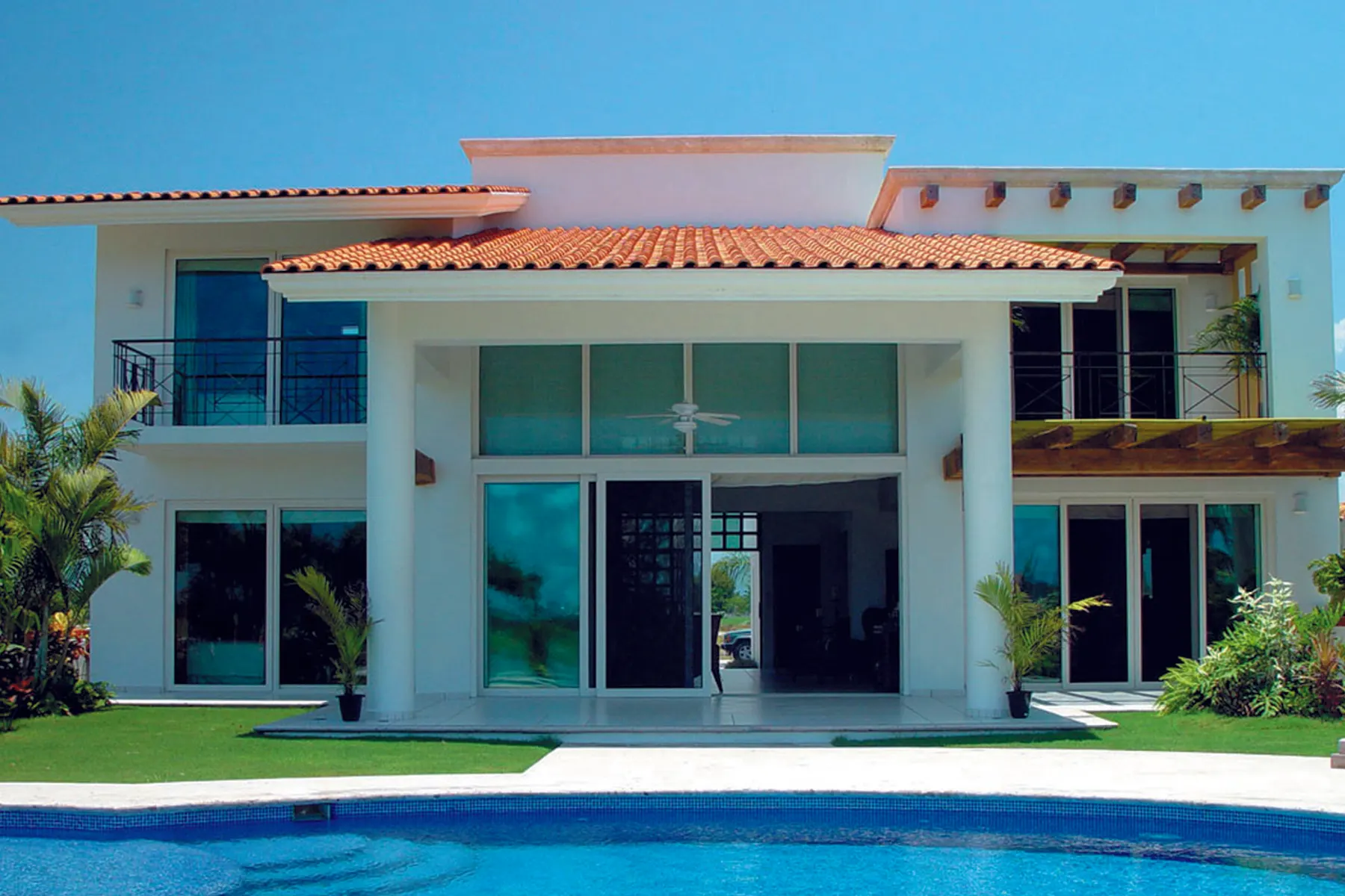 Vivienda unifamiliar con grandes paños acristalados en planta baja y primera, abierta a una piscina. En una fachada así, la orientación decide qué vidrio va en cada hueco.